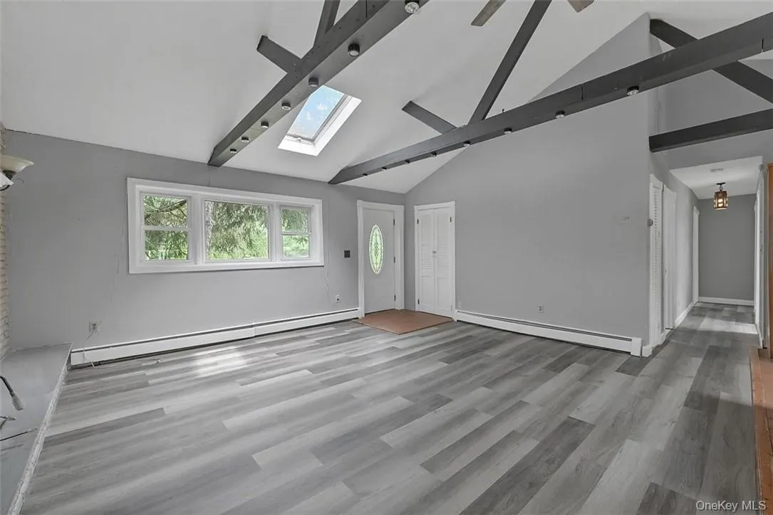 Unfurnished living room featuring beamed ceiling, a baseboard radiator, wood-type flooring, and a skylight Unfurnished living room featuring beamed ceiling, a baseboard radiator, wood-type flooring, and a skylight