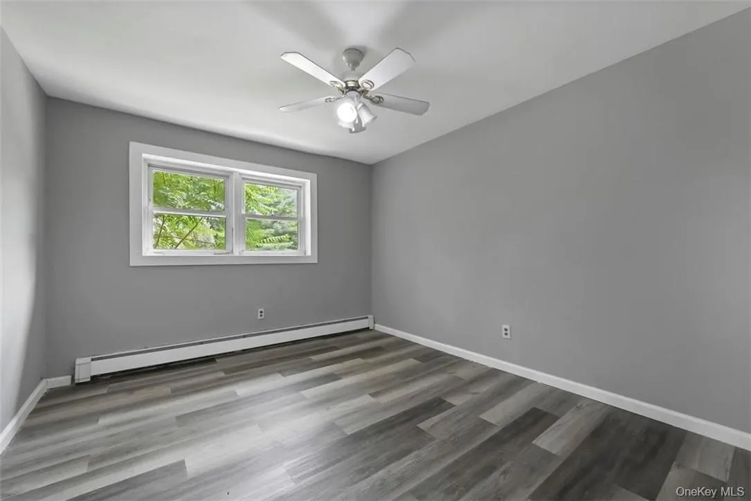 Empty room with a baseboard heating unit, hardwood / wood-style floors, and ceiling fan Empty room with a baseboard heating unit, hardwood / wood-style floors, and ceiling fan