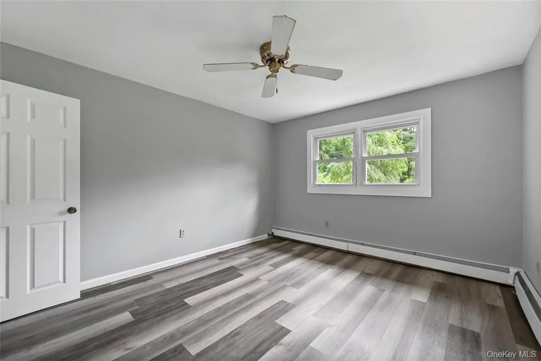 Empty room with ceiling fan, wood-type flooring, and baseboard heating Empty room with ceiling fan, wood-type flooring, and baseboard heating
