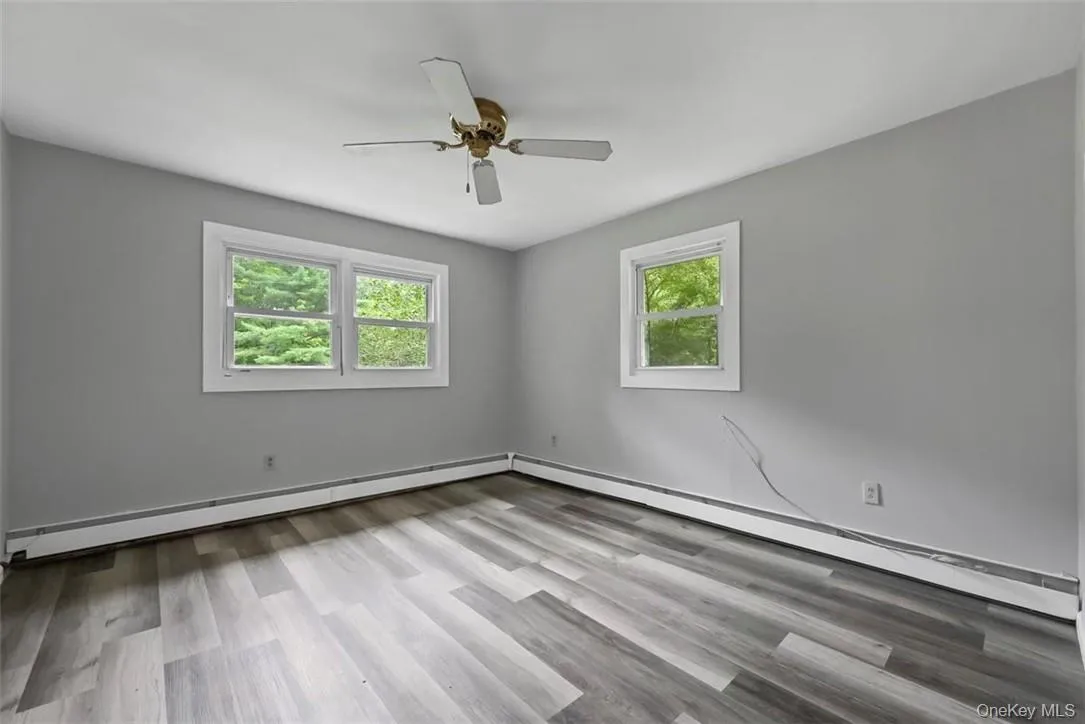 Unfurnished room with light wood-type flooring, ceiling fan, a wealth of natural light, and a baseboard heating unit Unfurnished room with light wood-type flooring, ceiling fan, a wealth of natural light, and a baseboard heating unit