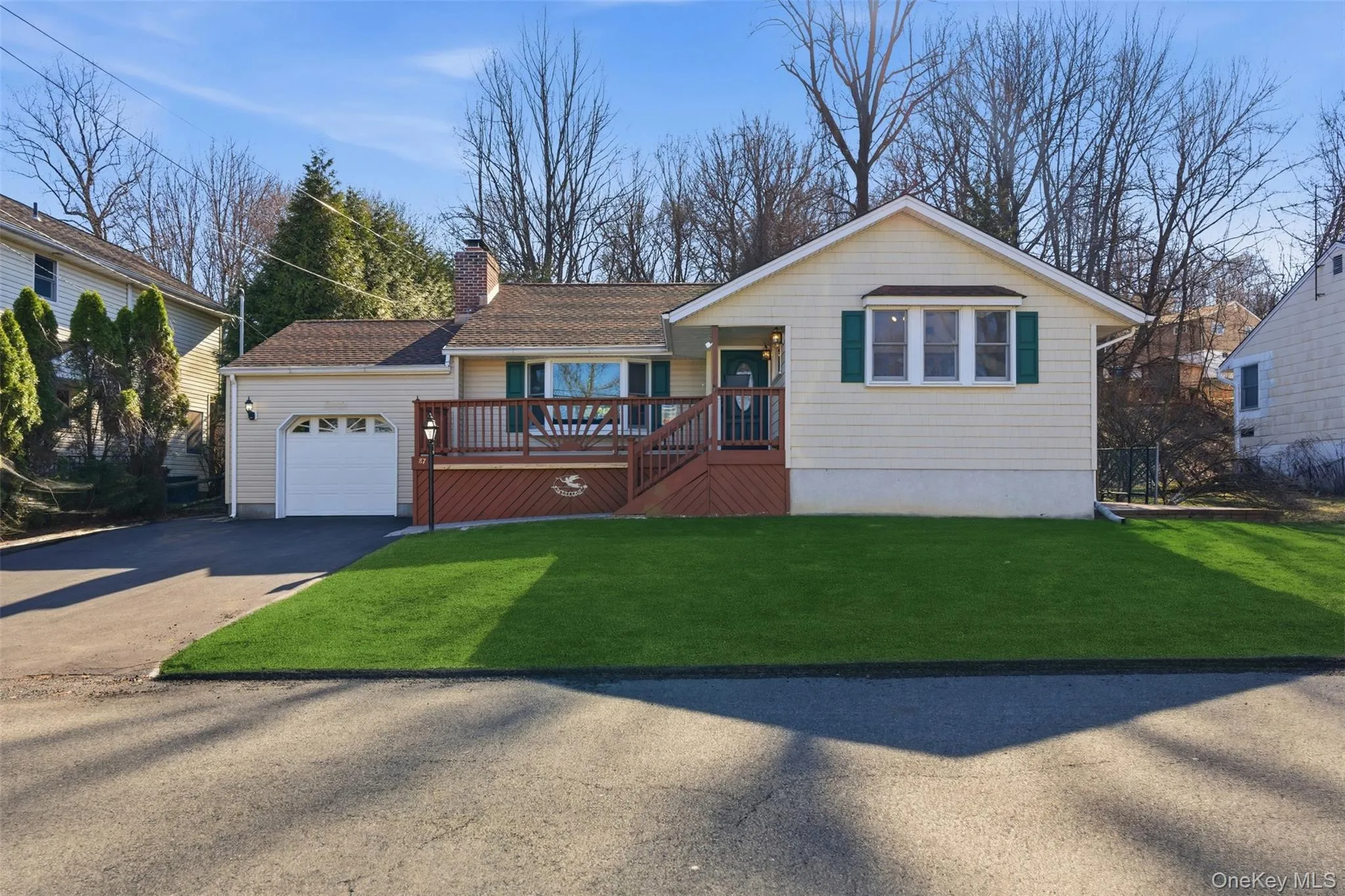 Ranch-style house with a wooden deck, an attached garage, driveway, a front yard, and a chimney Ranch-style house with a wooden deck, an attached garage, driveway, a front yard, and a chimney