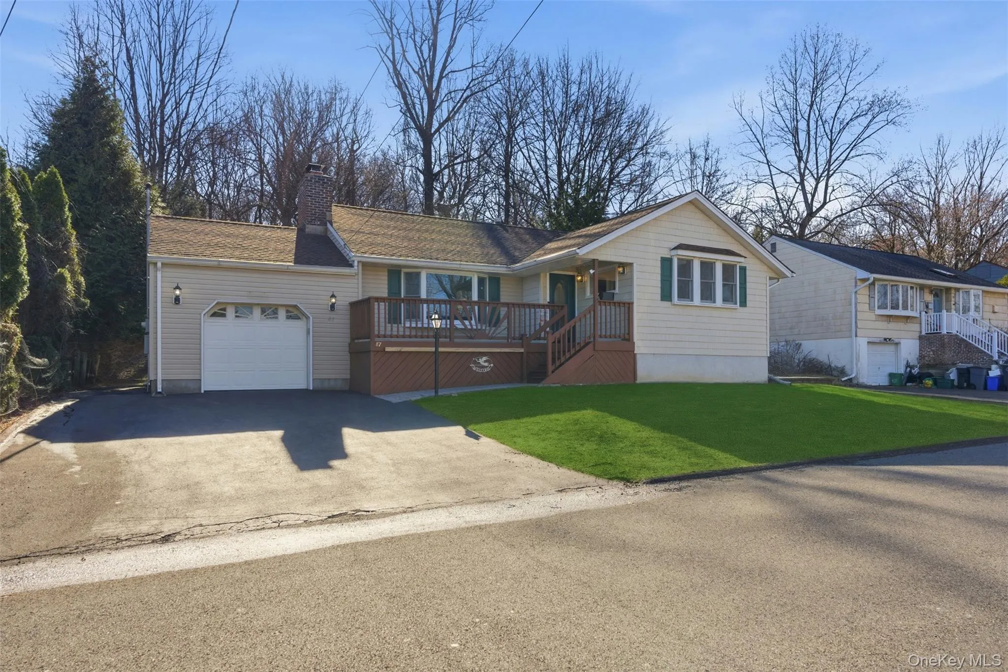 Ranch-style home featuring a wooden deck, a chimney, an attached garage, asphalt driveway, and a front yard Ranch-style home featuring a wooden deck, a chimney, an attached garage, asphalt driveway, and a front yard