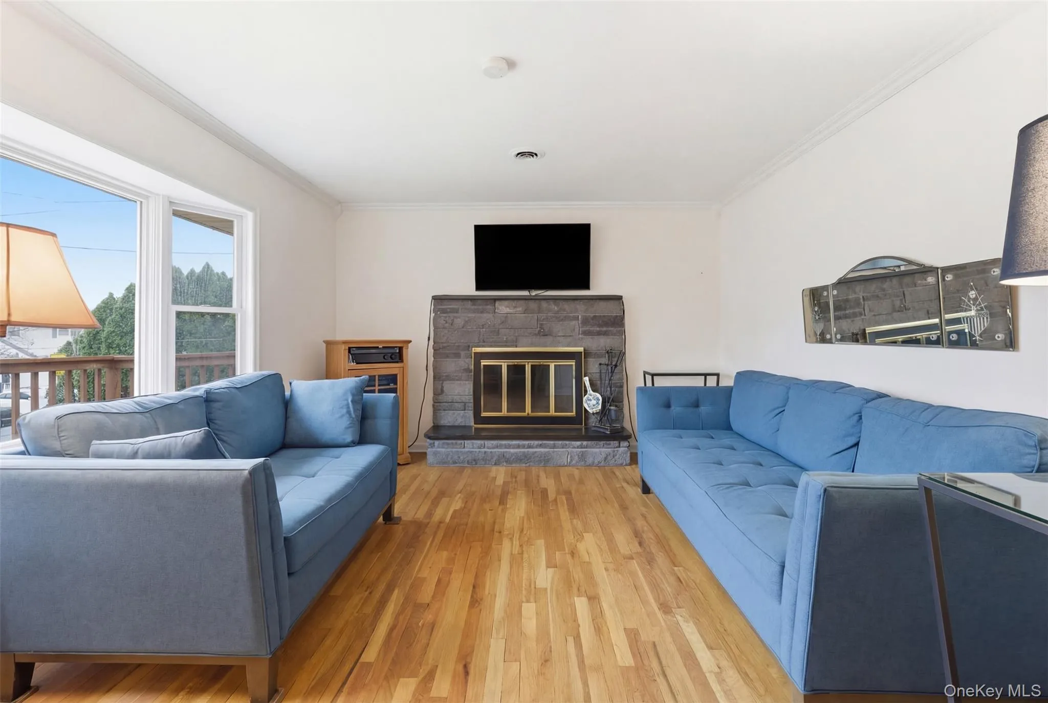 Living room with crown molding, light wood-style flooring, and a stone fireplace Living room with crown molding, light wood-style flooring, and a stone fireplace