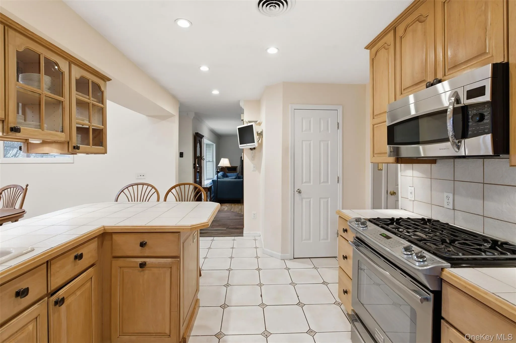 Kitchen featuring tile counters, stainless steel appliances, decorative backsplash, recessed lighting, and glass fronted cabinets Kitchen featuring tile counters, stainless steel appliances, decorative backsplash, recessed lighting, and glass fronted cabinets