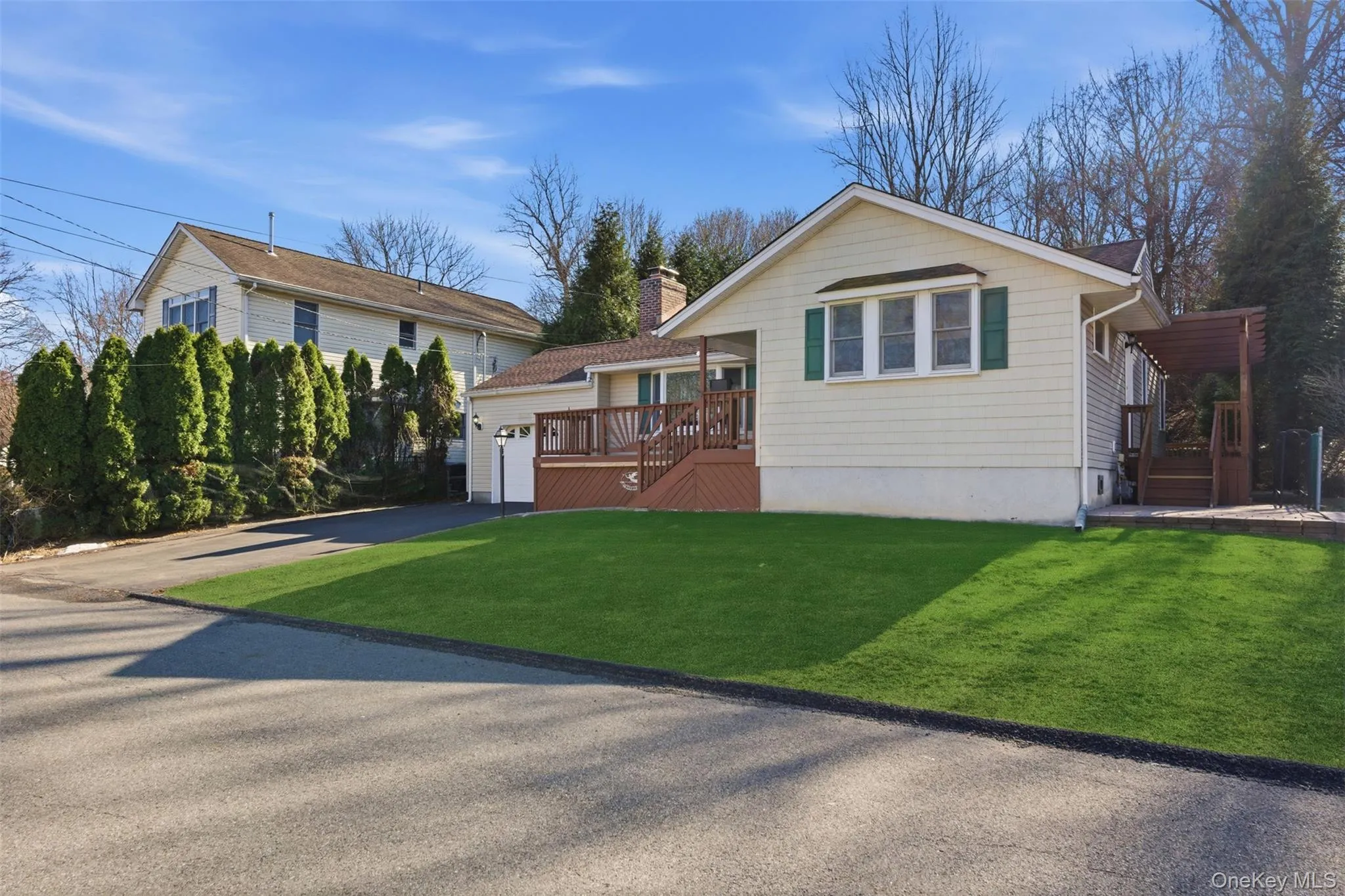 View of front of property with a deck, a front lawn, a chimney, asphalt driveway, and an attached garage View of front of property with a deck, a front lawn, a chimney, asphalt driveway, and an attached garage