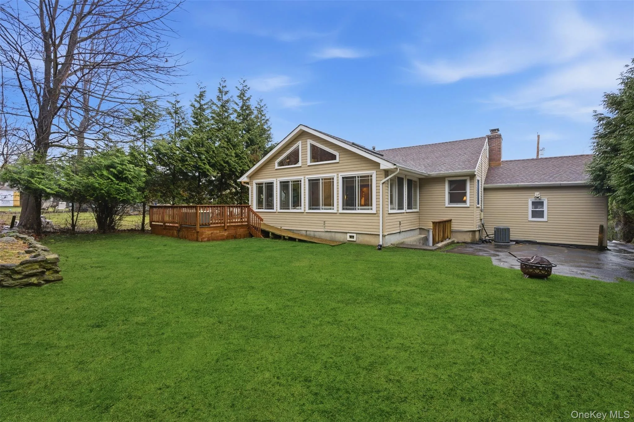 Rear view of house with a chimney, a deck, a lawn, and an outdoor fire pit Rear view of house with a chimney, a deck, a lawn, and an outdoor fire pit