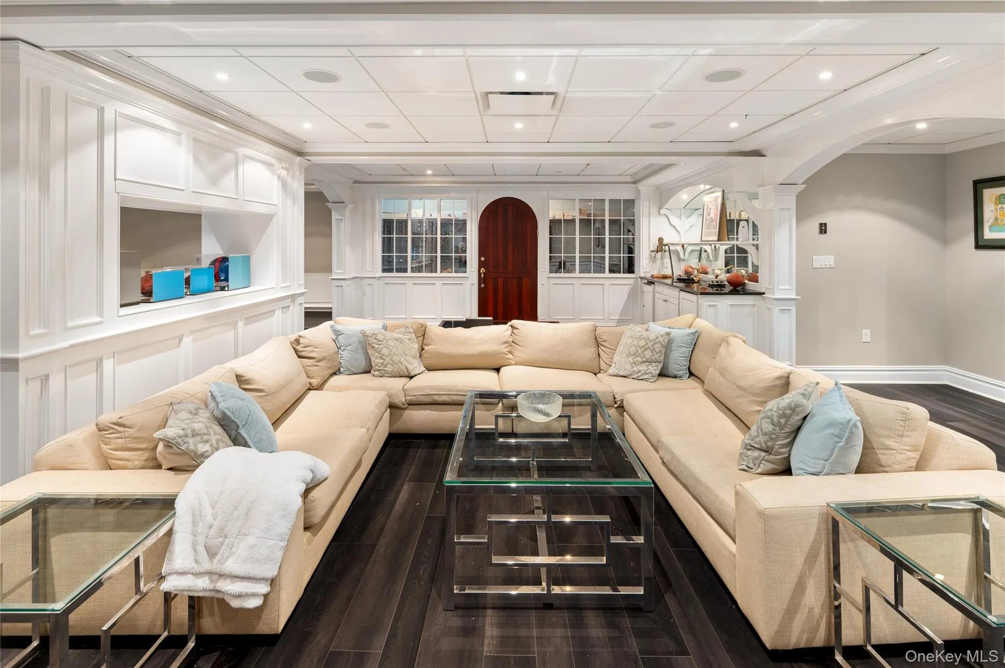 Living area with arched walkways, ornate columns, dark wood-style floors, crown molding, and recessed lighting Living area with arched walkways, ornate columns, dark wood-style floors, crown molding, and recessed lighting