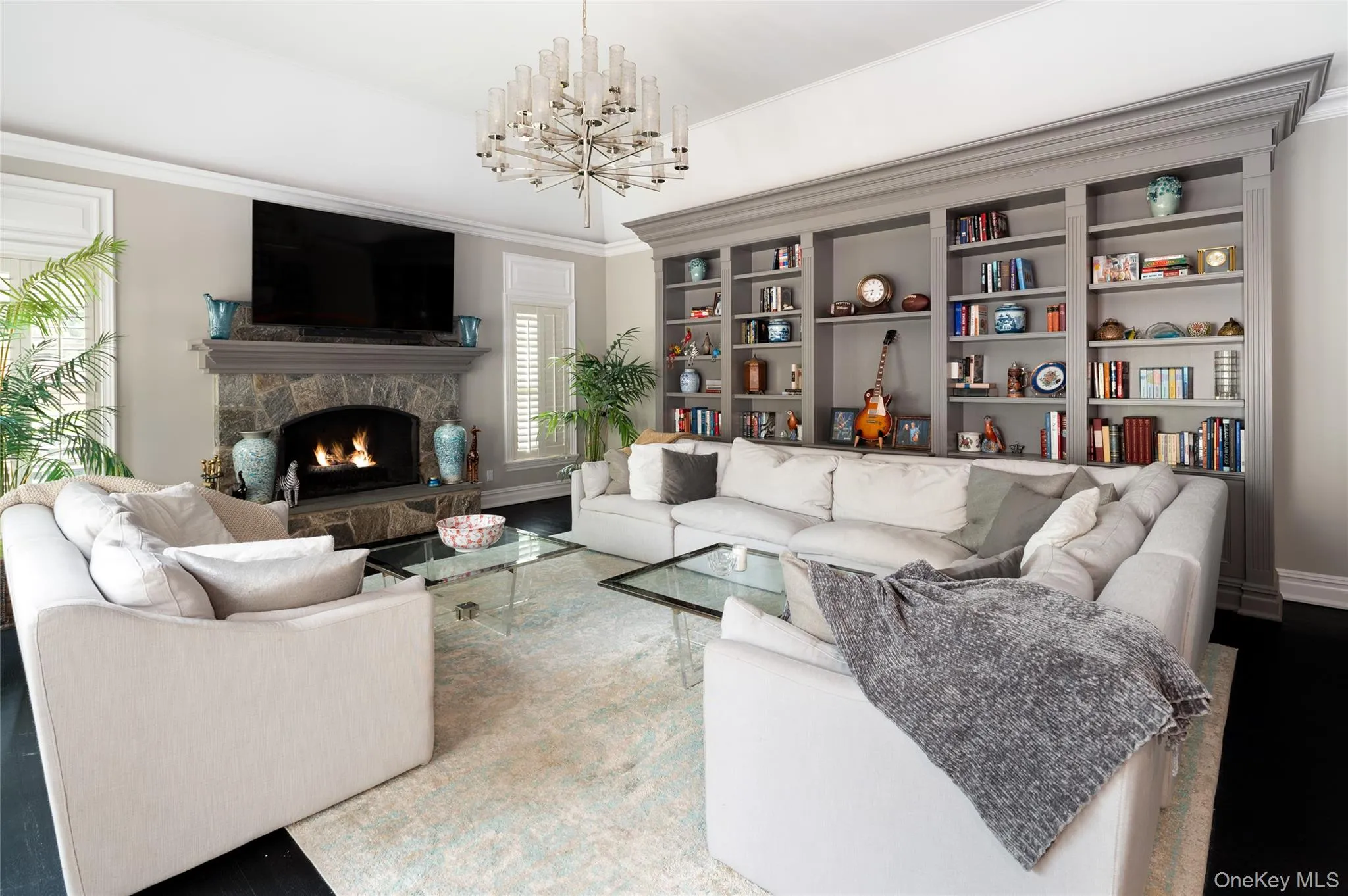 Living room featuring a chandelier, crown molding, a stone fireplace, and baseboards Living room featuring a chandelier, crown molding, a stone fireplace, and baseboards