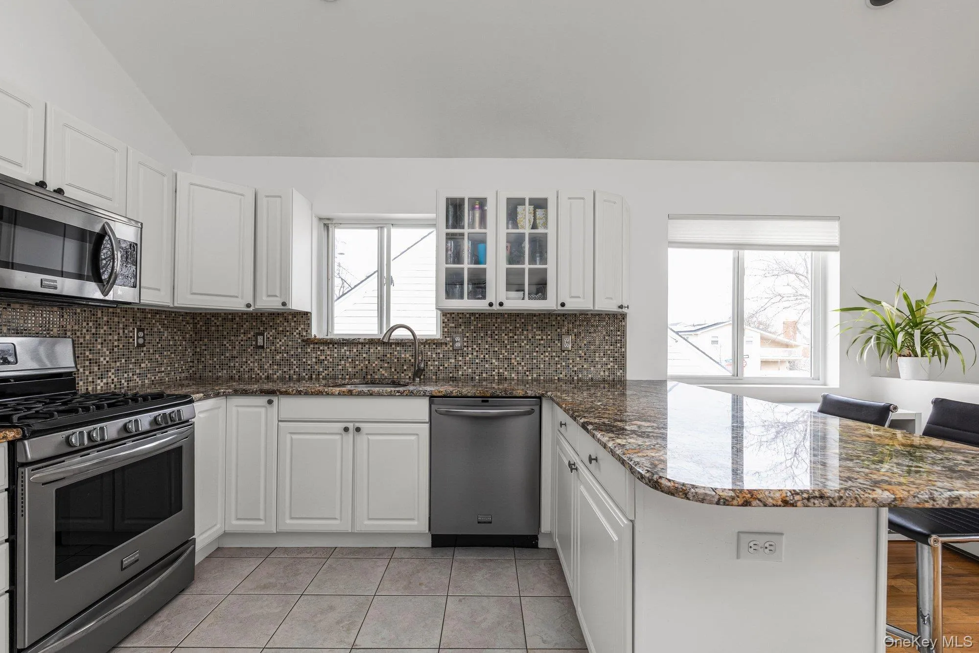 Kitchen with stainless steel appliances, a breakfast bar area, dark stone counters, white cabinetry, and vaulted ceiling Kitchen with stainless steel appliances, a breakfast bar area, dark stone counters, white cabinetry, and vaulted ceiling