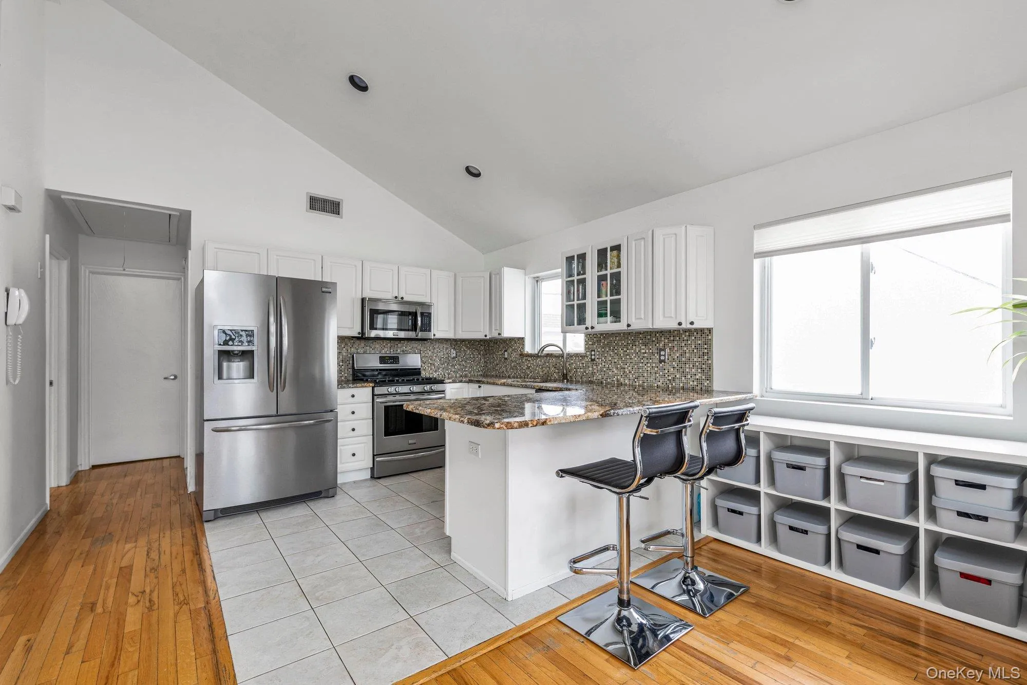 Kitchen with stainless steel appliances, a peninsula, vaulted ceiling, light wood-style flooring, and white cabinetry Kitchen with stainless steel appliances, a peninsula, vaulted ceiling, light wood-style flooring, and white cabinetry