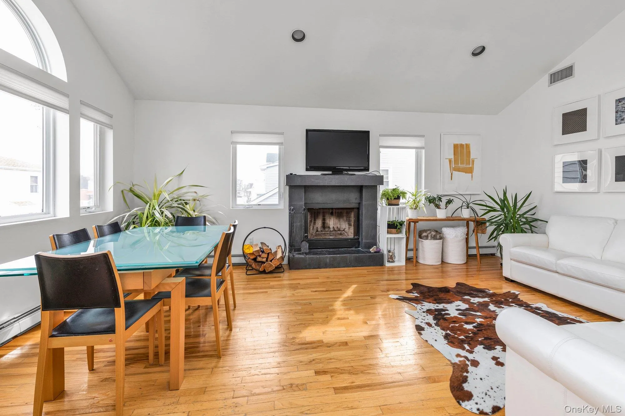 Living room featuring lofted ceiling, light wood-type flooring, a fireplace, and baseboard heating Living room featuring lofted ceiling, light wood-type flooring, a fireplace, and baseboard heating