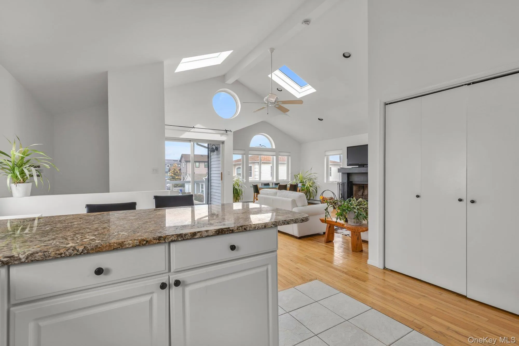 Kitchen featuring a skylight, light tile patterned flooring, white cabinets, dark stone counters, and a fireplace Kitchen featuring a skylight, light tile patterned flooring, white cabinets, dark stone counters, and a fireplace