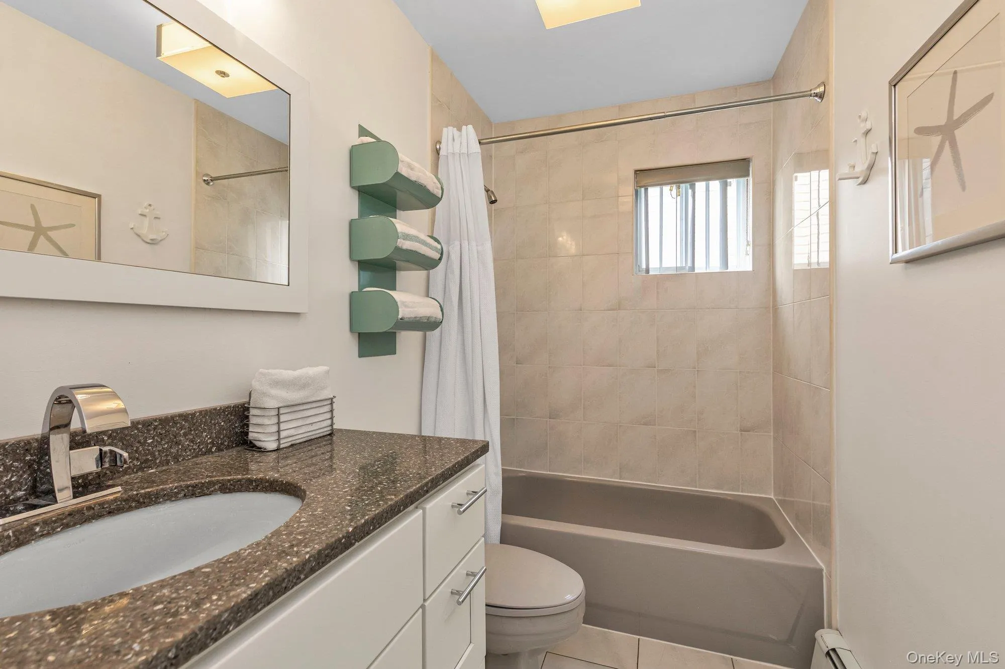Full bath featuring vanity, shower / bathtub combination with curtain, a baseboard heating unit, and light tile patterned floors Full bath featuring vanity, shower / bathtub combination with curtain, a baseboard heating unit, and light tile patterned floors