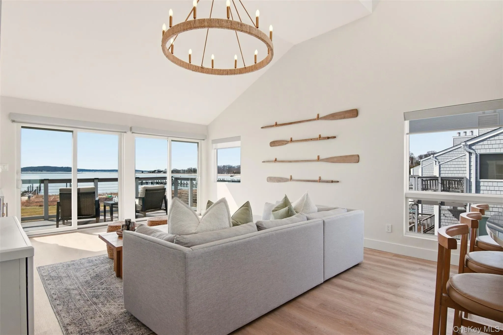 Living area with light wood finished floors, suspended lighting, wine cooler, vaulted ceiling, and built in shelves - incredible views of Gardiner's Bay through windows and double sliding doors that lead to balcony. Living area with light wood finished floors, suspended lighting, wine cooler, vaulted ceiling, and built in shelves - incredible views of Gardiner's Bay through windows and double sliding doors that lead to balcony.