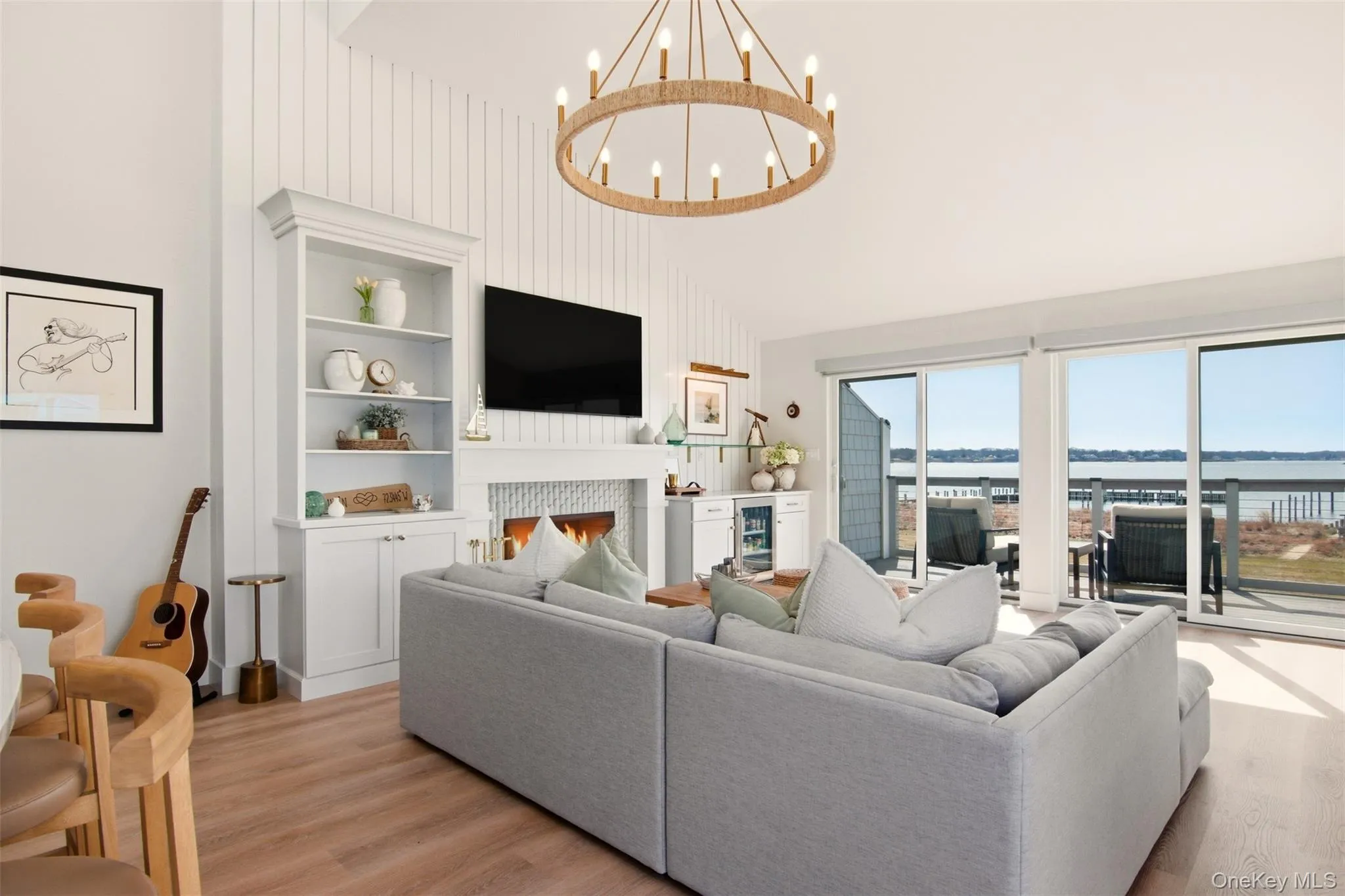 Living area with light wood finished floors, suspended lighting, wine cooler, vaulted ceiling, and built in shelves - incredible views of Gardiner's Bay through windows and double sliding doors that lead to balcony. Living area with light wood finished floors, suspended lighting, wine cooler, vaulted ceiling, and built in shelves - incredible views of Gardiner's Bay through windows and double sliding doors that lead to balcony.