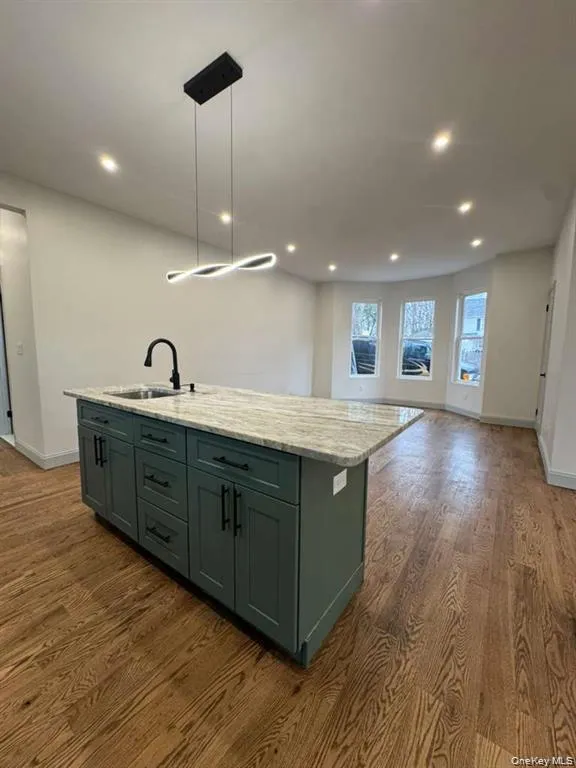 Kitchen featuring a kitchen island with sink, dark wood-style floors, light stone counters, open floor plan, and hanging light fixtures Kitchen featuring a kitchen island with sink, dark wood-style floors, light stone counters, open floor plan, and hanging light fixtures