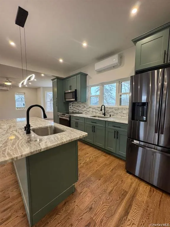 Kitchen featuring green cabinets, light stone countertops, stainless steel appliances, and pendant lighting Kitchen featuring green cabinets, light stone countertops, stainless steel appliances, and pendant lighting