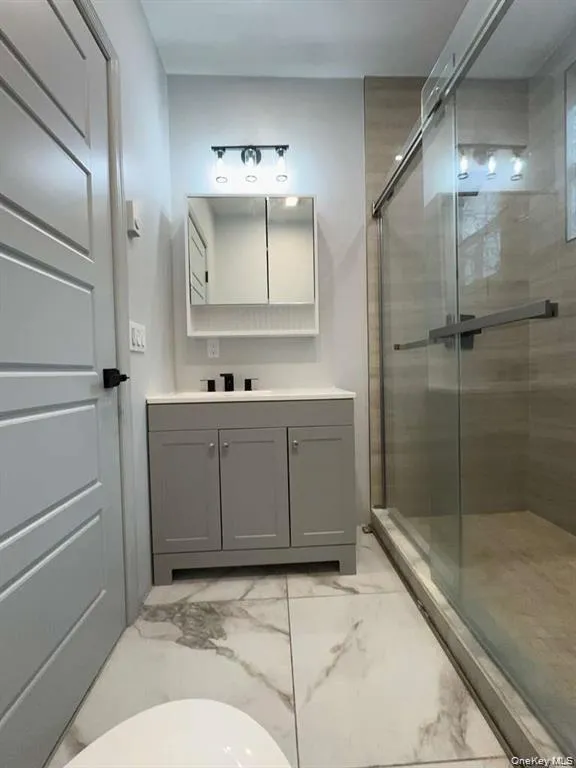 Bathroom featuring a stall shower, vanity, and light marble finish flooring Bathroom featuring a stall shower, vanity, and light marble finish flooring