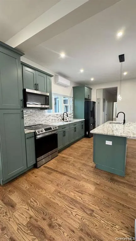 Kitchen featuring green cabinets, stainless steel appliances, hanging light fixtures, dark wood finished floors, and light stone countertops Kitchen featuring green cabinets, stainless steel appliances, hanging light fixtures, dark wood finished floors, and light stone countertops