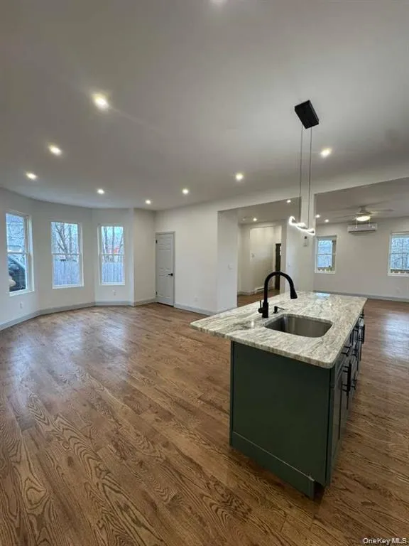 Kitchen with open floor plan, a center island with sink, light stone countertops, decorative light fixtures, and dark wood-type flooring Kitchen with open floor plan, a center island with sink, light stone countertops, decorative light fixtures, and dark wood-type flooring