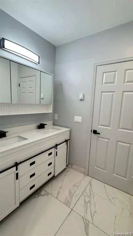 Bathroom featuring double vanity and light marble finish floors Bathroom featuring double vanity and light marble finish floors