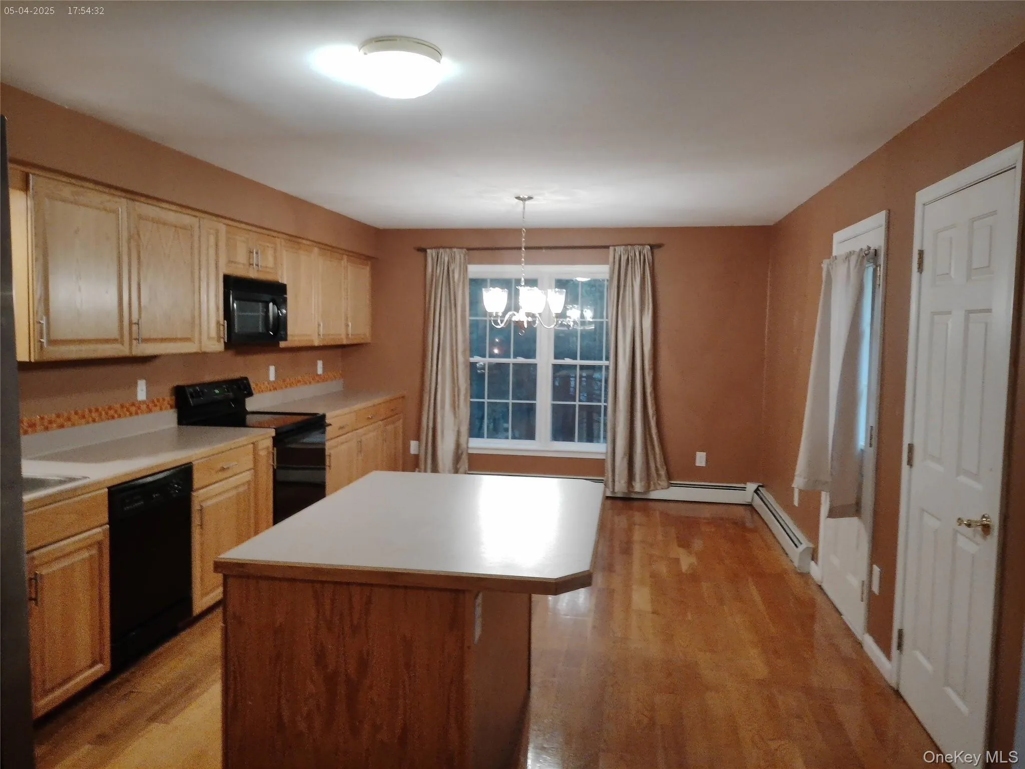 Kitchen featuring light countertops, light wood-style flooring, light brown cabinets, black appliances, and an inviting chandelier Kitchen featuring light countertops, light wood-style flooring, light brown cabinets, black appliances, and an inviting chandelier