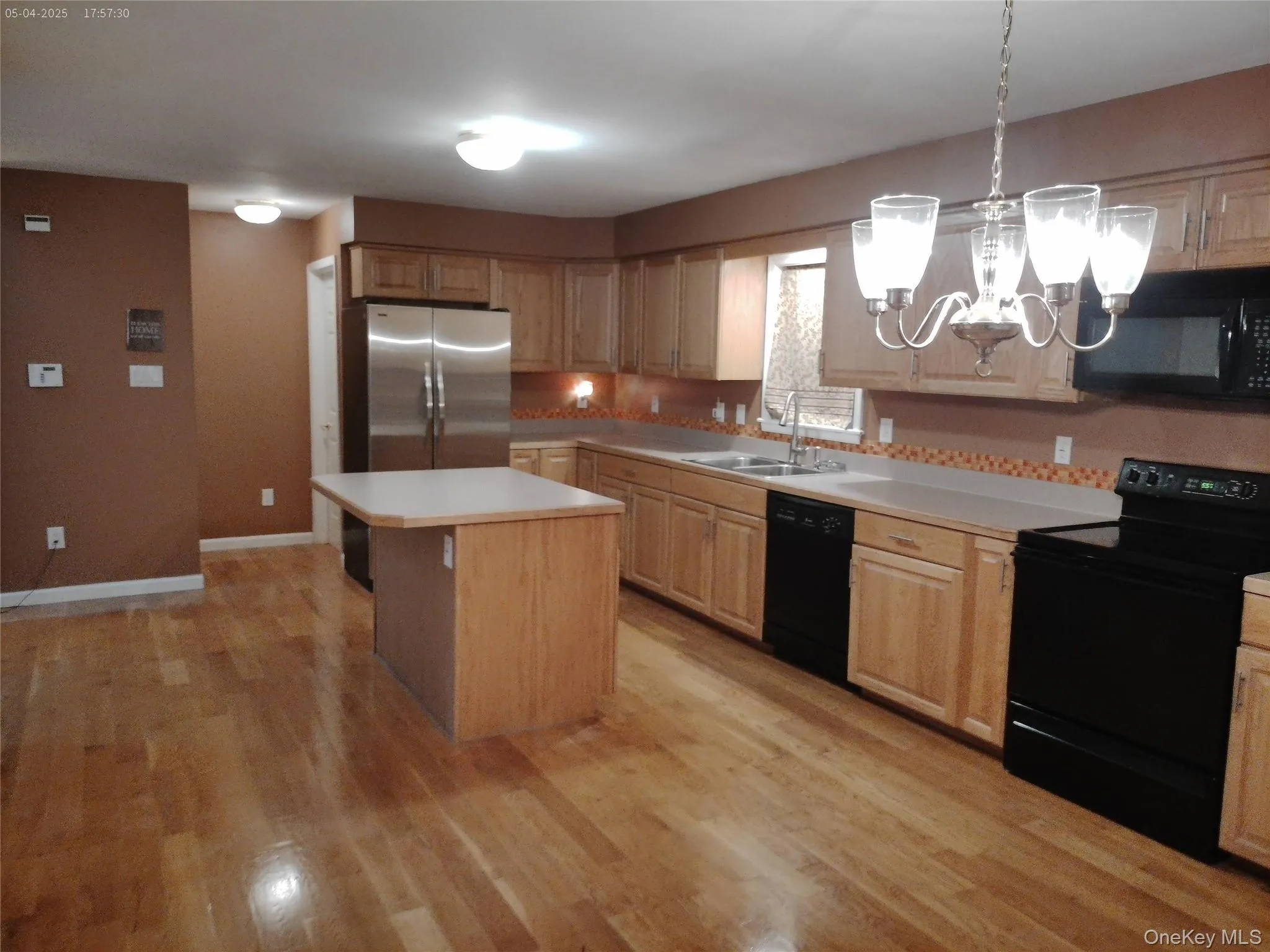 Kitchen featuring light countertops, light wood finished floors, a sink, black appliances, and a notable chandelier Kitchen featuring light countertops, light wood finished floors, a sink, black appliances, and a notable chandelier