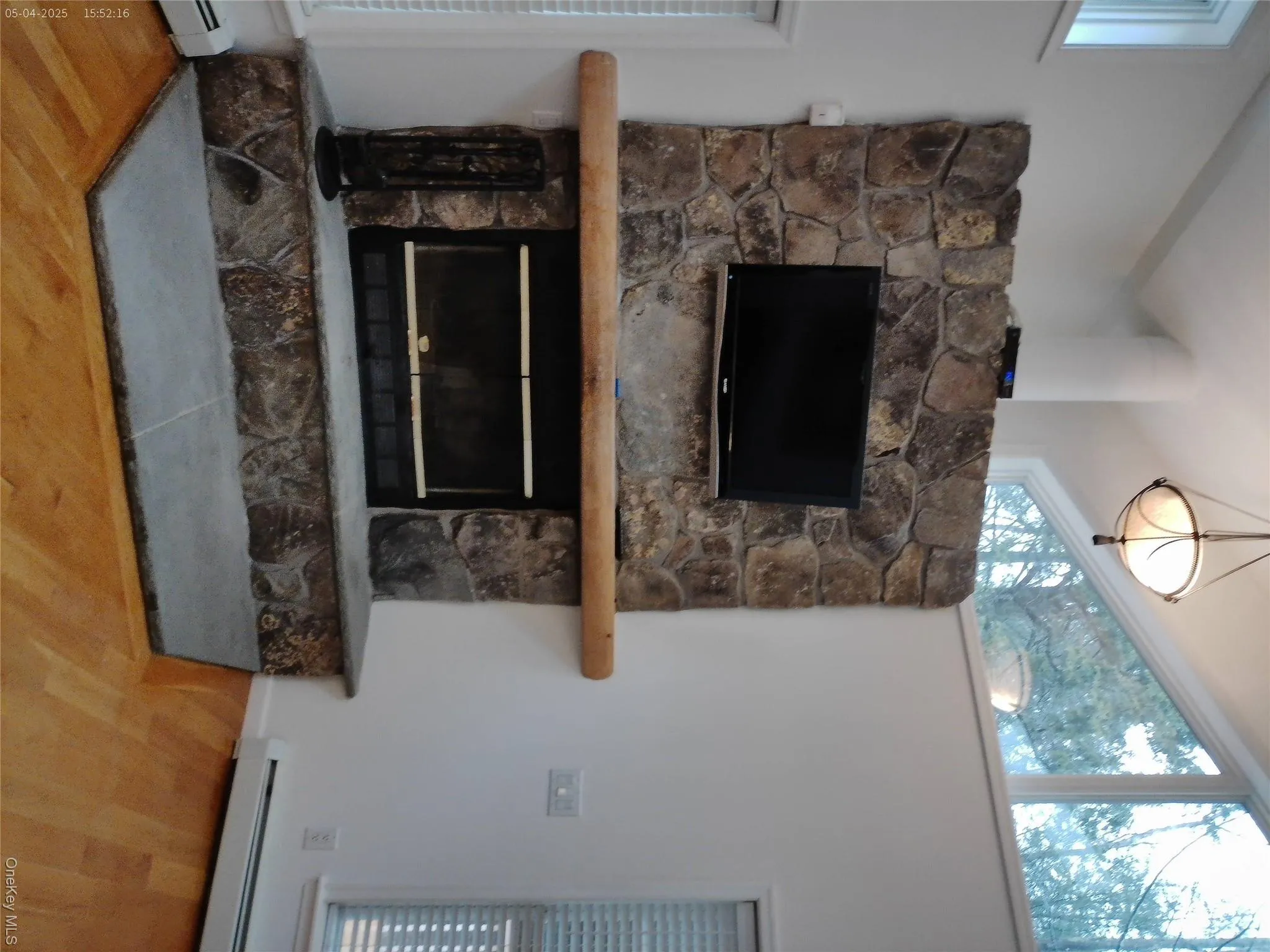 Room details with a stone fireplace, a baseboard heating unit, and wood finished floors Room details with a stone fireplace, a baseboard heating unit, and wood finished floors