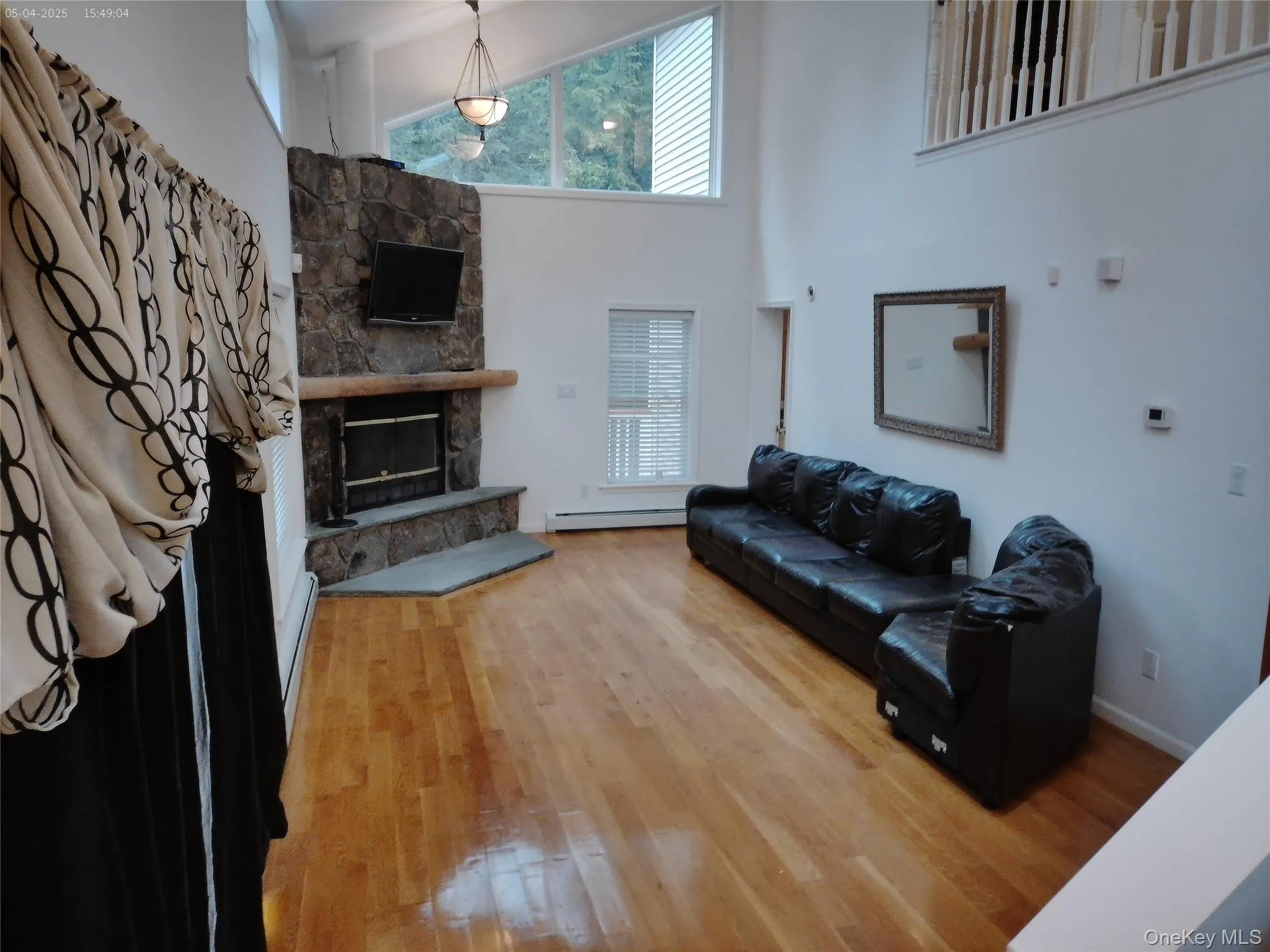 Living area featuring baseboards, a towering ceiling, a baseboard radiator, a stone fireplace, and wood finished floors Living area featuring baseboards, a towering ceiling, a baseboard radiator, a stone fireplace, and wood finished floors