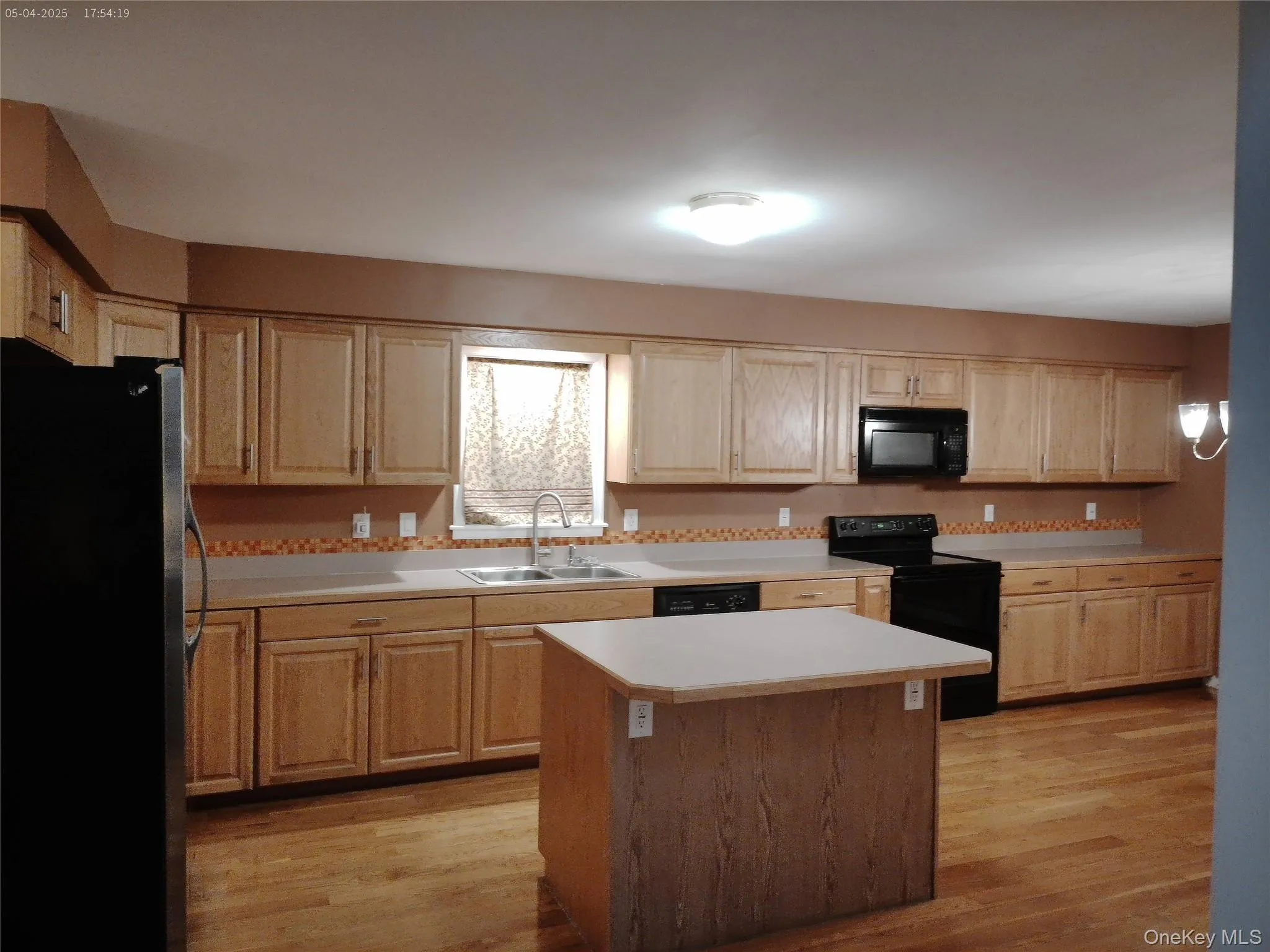 Kitchen featuring light wood finished floors, black appliances, light countertops, and a sink Kitchen featuring light wood finished floors, black appliances, light countertops, and a sink