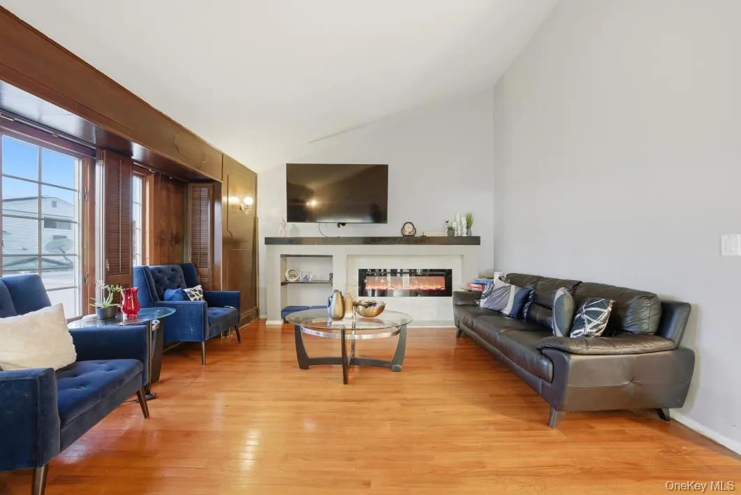 Living area featuring a glass covered fireplace, light wood finished floors, and vaulted ceiling Living area featuring a glass covered fireplace, light wood finished floors, and vaulted ceiling