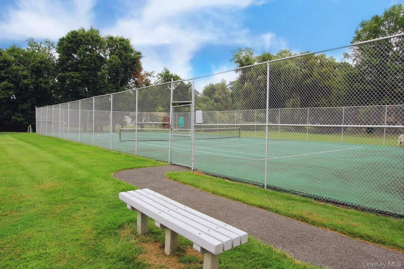 View of tennis court with green space and seating. View of tennis court with green space and seating.