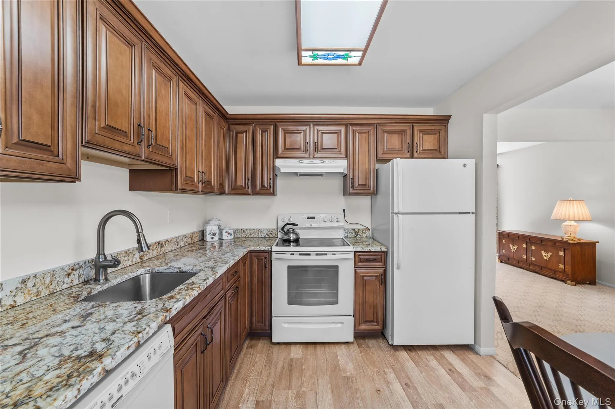 Kitchen featuring light granite counters, under cabinet range hood, a stainless sink with designer faucets and light wood-type flooring Kitchen featuring light granite counters, under cabinet range hood, a stainless sink with designer faucets and light wood-type flooring