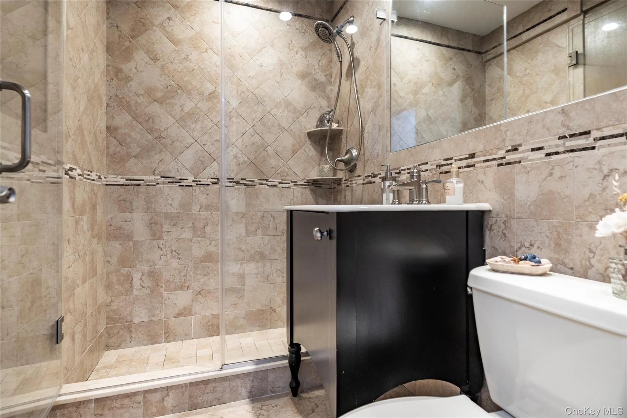 Bathroom with toilet, vanity, a stall shower, and tile walls Bathroom with toilet, vanity, a stall shower, and tile walls