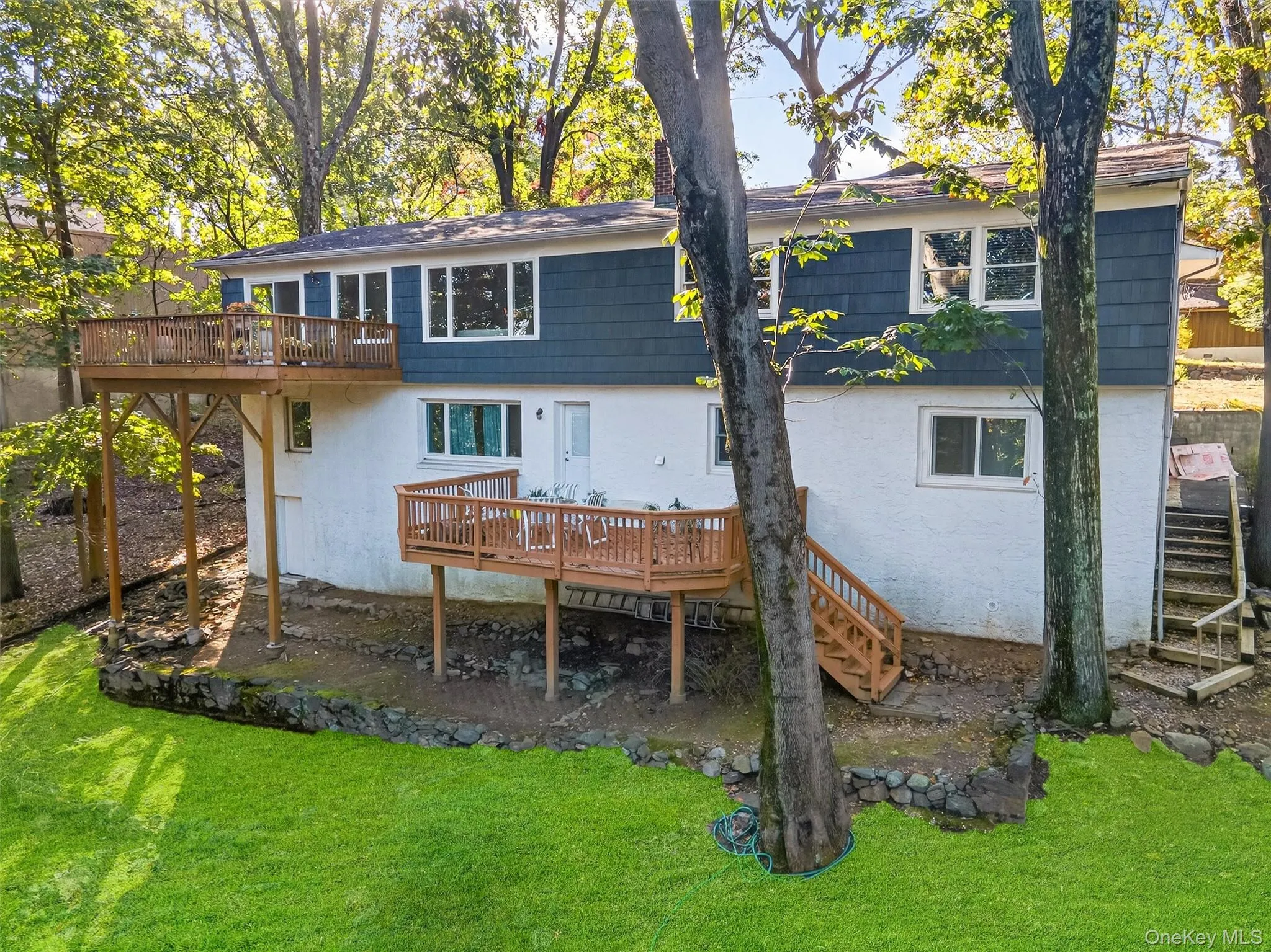 Lower Level view of house with stairway, a deck, a lawn, and stucco siding Lower Level view of house with stairway, a deck, a lawn, and stucco siding