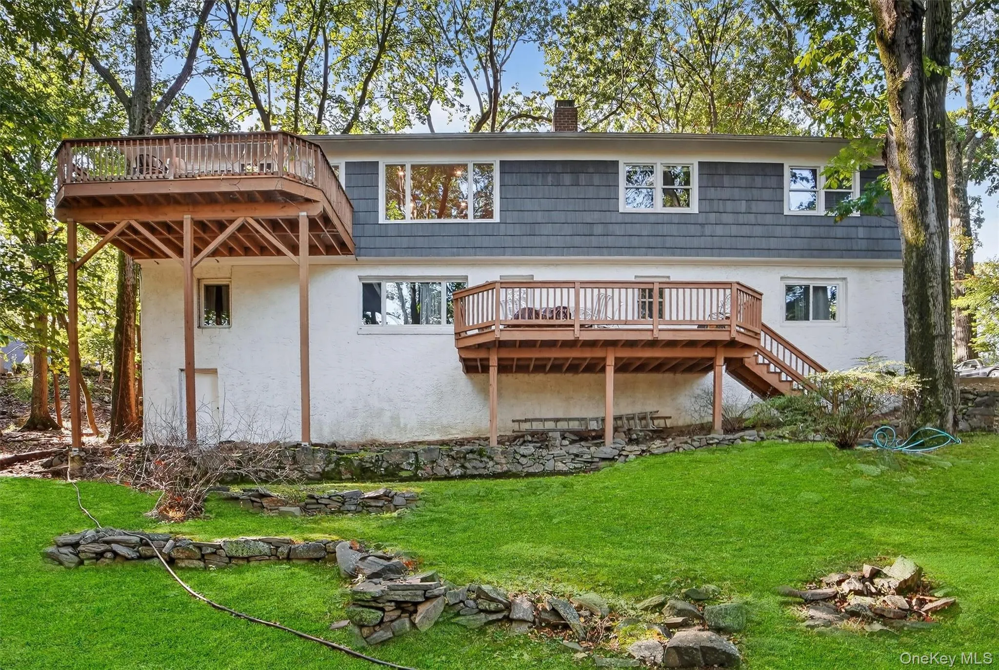 Back of house featuring stairs, a chimney, stucco siding, a wooden deck, and a lawn Back of house featuring stairs, a chimney, stucco siding, a wooden deck, and a lawn