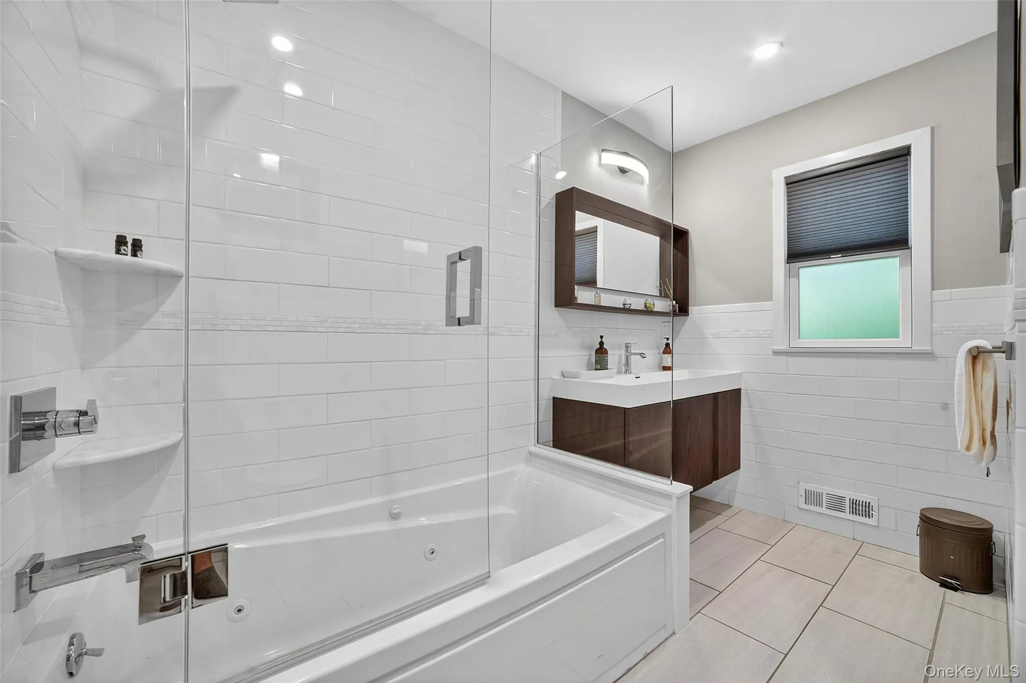 Full bathroom with tile walls, vanity, light tile patterned floors, wainscoting, and a combined bath / shower with jetted tub Full bathroom with tile walls, vanity, light tile patterned floors, wainscoting, and a combined bath / shower with jetted tub