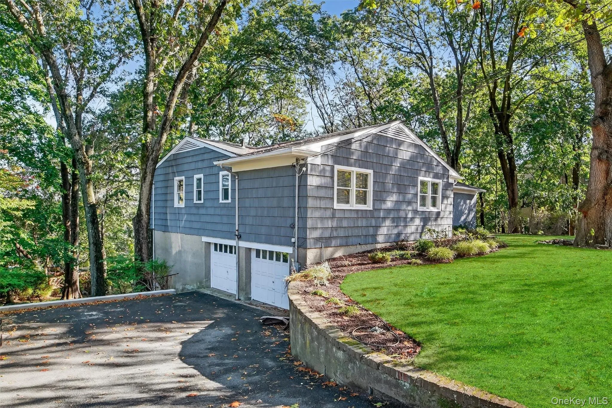 View of side of property with an attached garage, asphalt driveway, view of wooded area, and a lawn View of side of property with an attached garage, asphalt driveway, view of wooded area, and a lawn