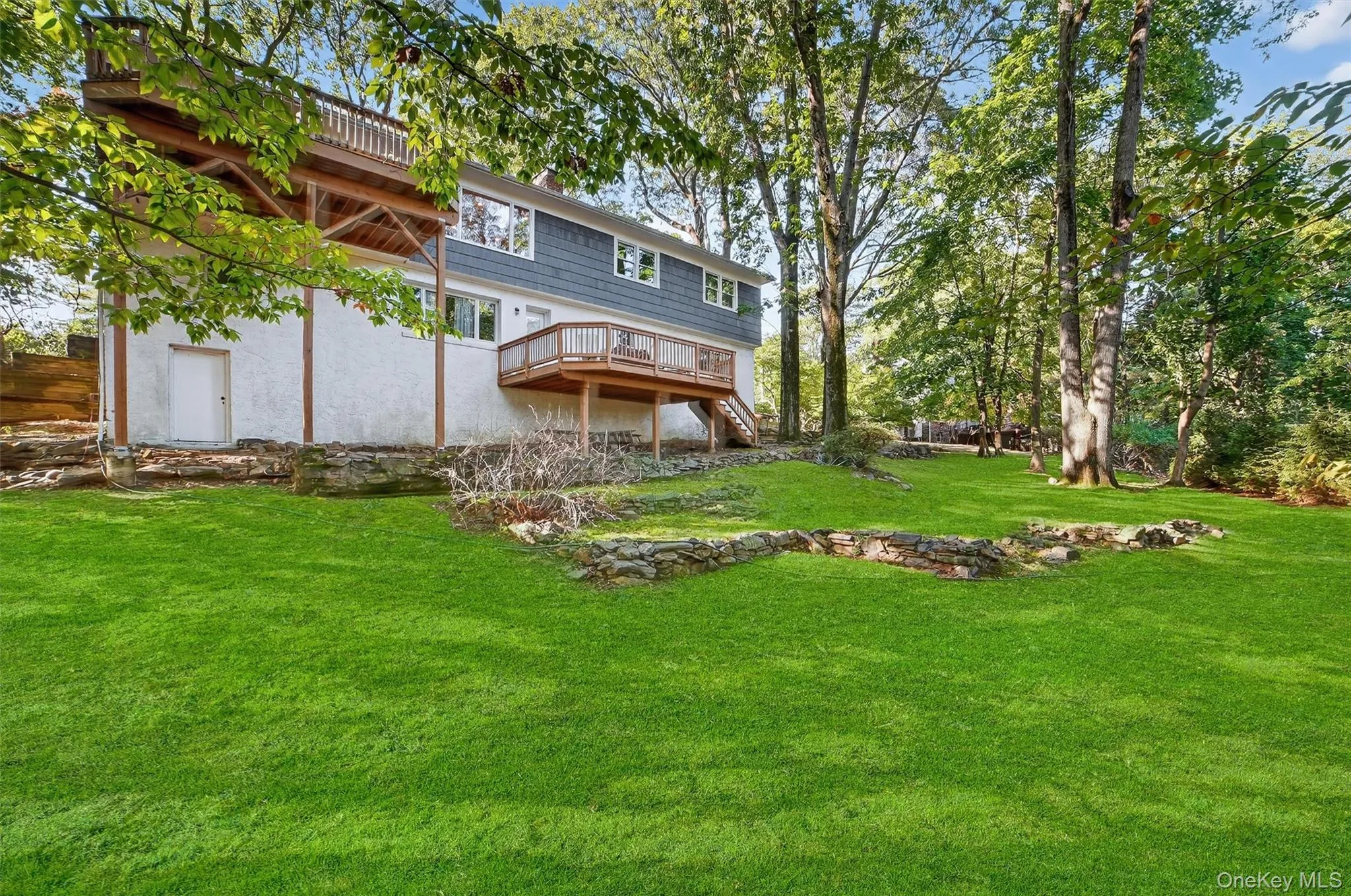 Back of property featuring a wooden deck, stairs, a yard, and stucco siding Back of property featuring a wooden deck, stairs, a yard, and stucco siding