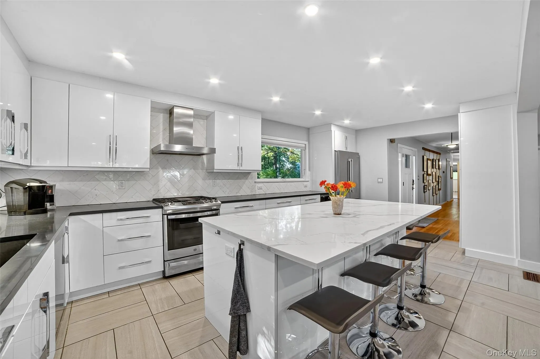 Kitchen with a breakfast bar area, stainless steel appliances, dark stone countertops, wall chimney range hood, and recessed lighting Kitchen with a breakfast bar area, stainless steel appliances, dark stone countertops, wall chimney range hood, and recessed lighting