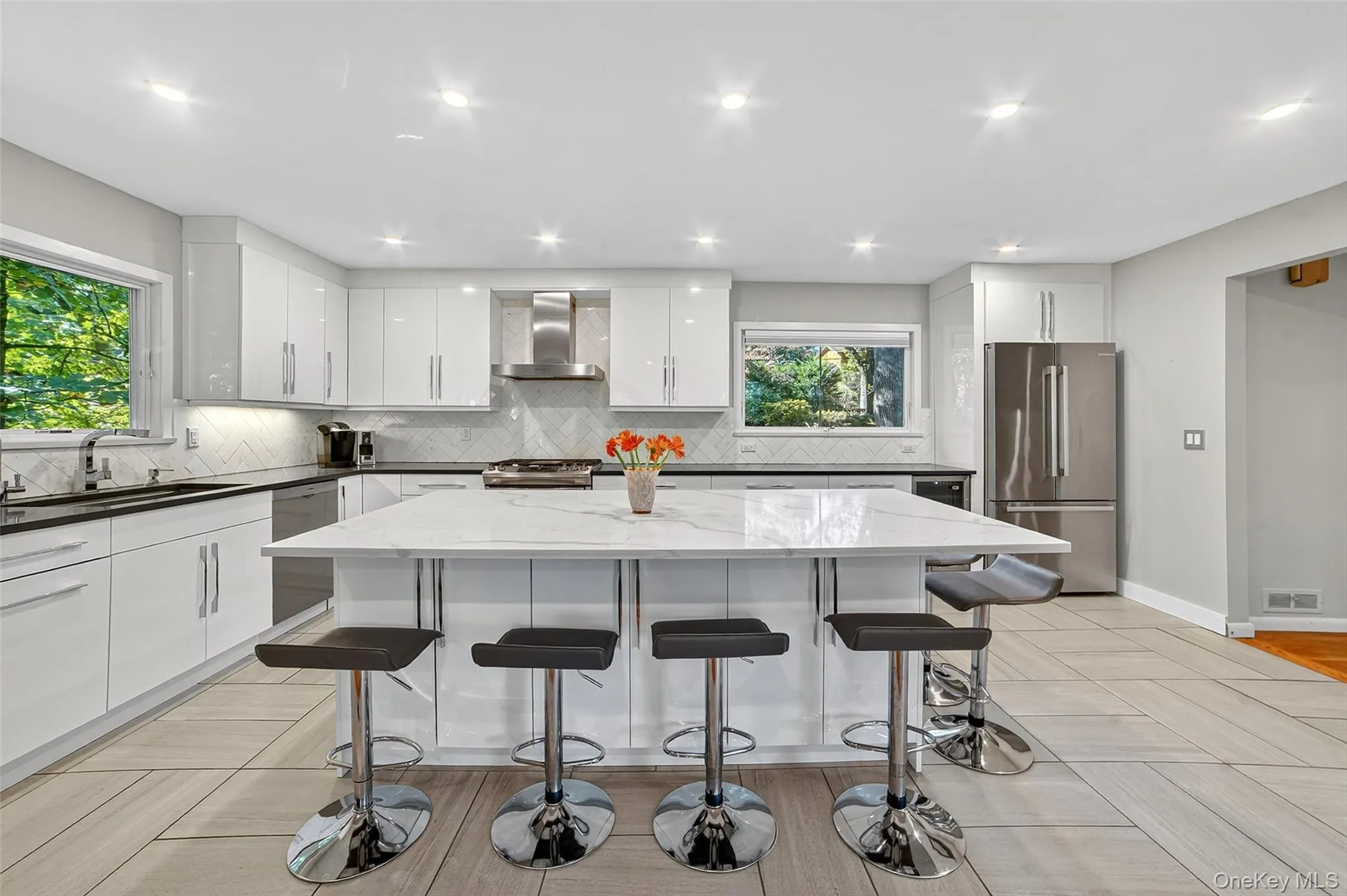 Kitchen featuring dark stone countertops, white cabinets, stainless steel appliances, a kitchen breakfast bar, and wall chimney exhaust hood Kitchen featuring dark stone countertops, white cabinets, stainless steel appliances, a kitchen breakfast bar, and wall chimney exhaust hood