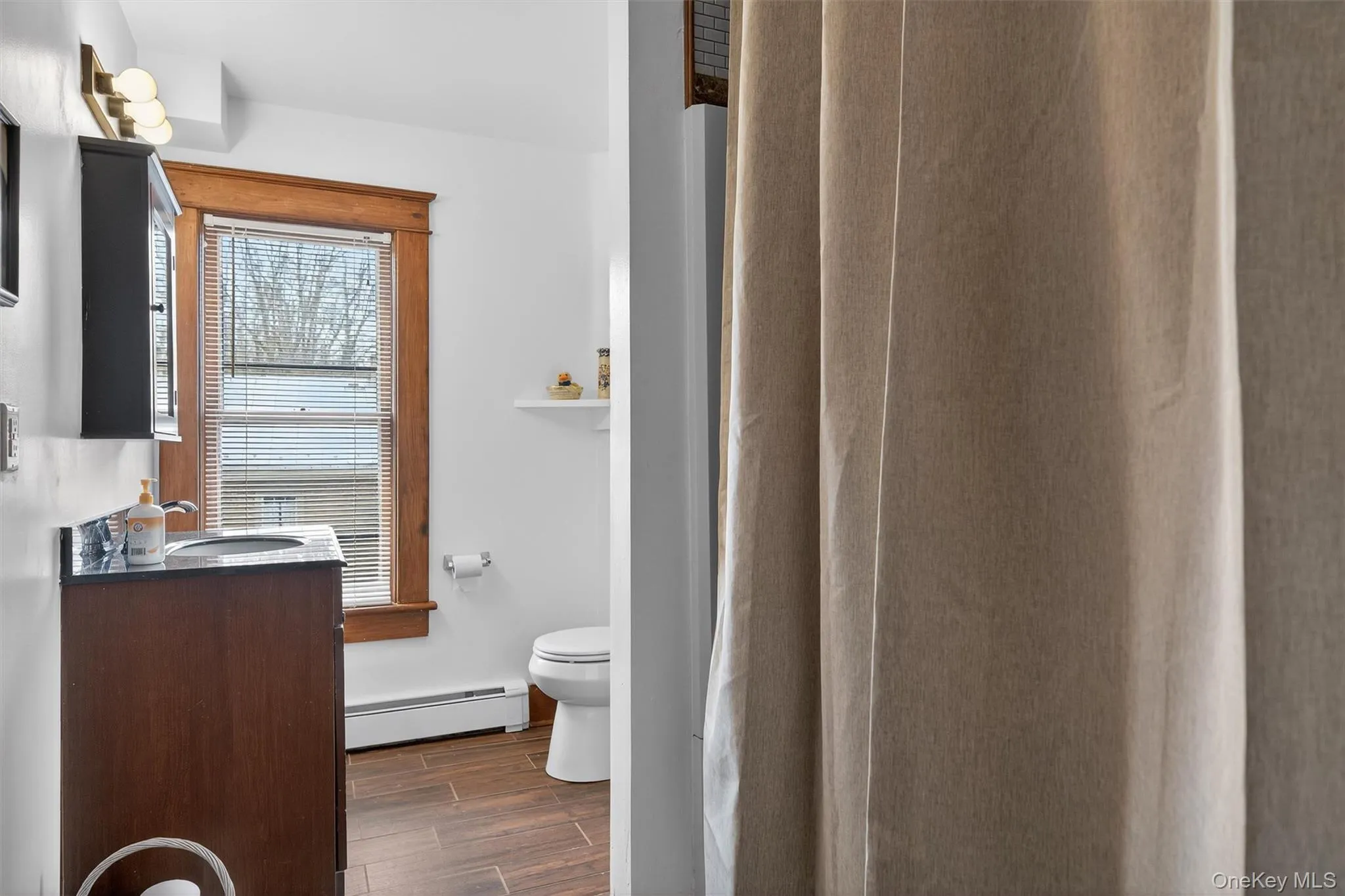 Full bath featuring vanity, a shower with shower curtain, wood finish floors, and a baseboard heating unit Full bath featuring vanity, a shower with shower curtain, wood finish floors, and a baseboard heating unit