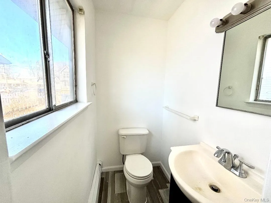 Primary half bath featuring a baseboard heating unit, healthy amount of natural light, vanity, and vinyl wood-style floors Primary half bath featuring a baseboard heating unit, healthy amount of natural light, vanity, and vinyl wood-style floors