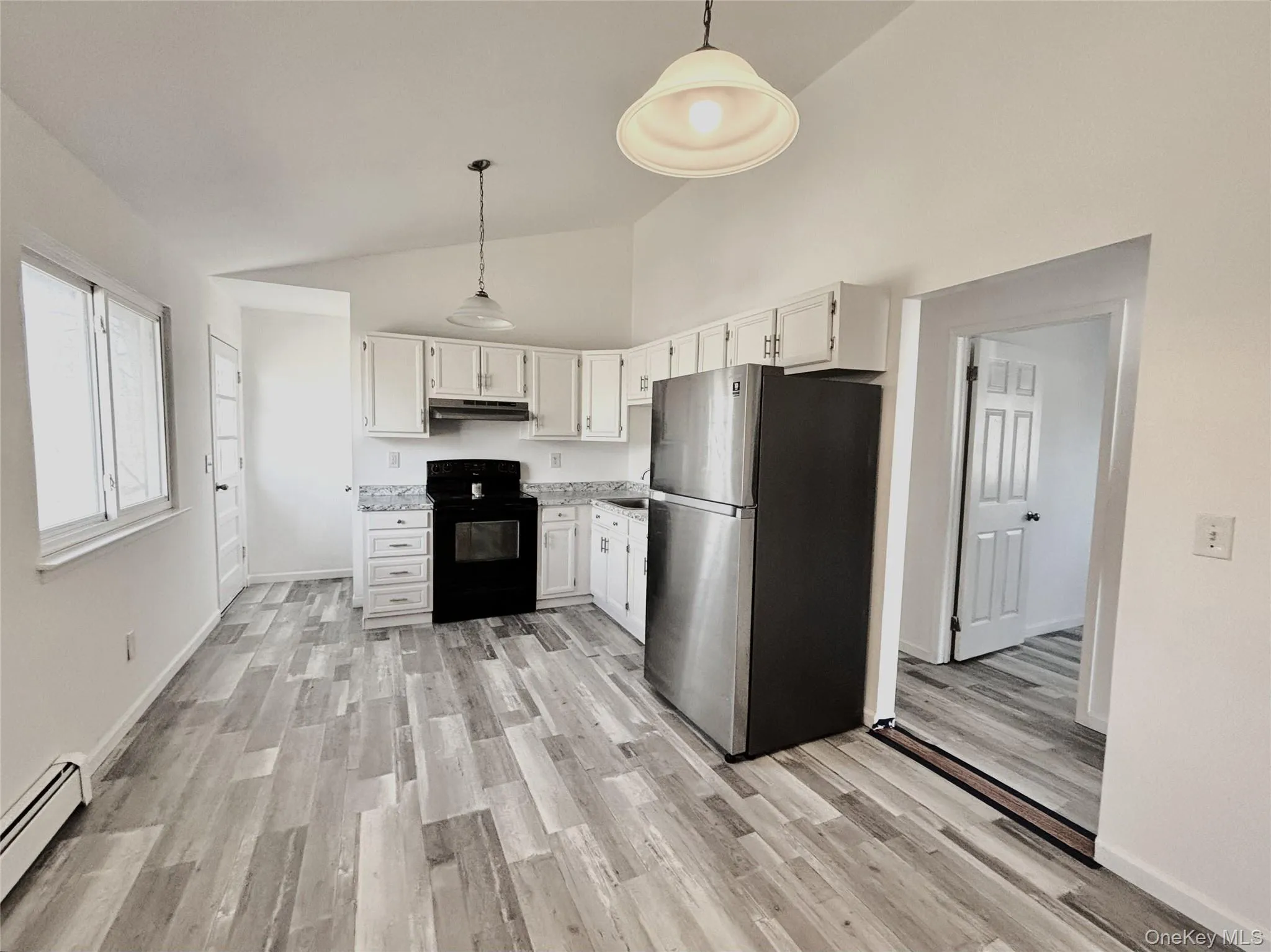 Kitchen featuring freestanding refrigerator, black range with electric stovetop, pendant lighting, white cabinets, vaulted ceiling and side entrance Kitchen featuring freestanding refrigerator, black range with electric stovetop, pendant lighting, white cabinets, vaulted ceiling and side entrance