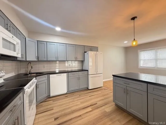 Kitchen featuring gray cabinetry, white appliances, light wood-type flooring, hanging light fixtures, and tasteful backsplash Kitchen featuring gray cabinetry, white appliances, light wood-type flooring, hanging light fixtures, and tasteful backsplash