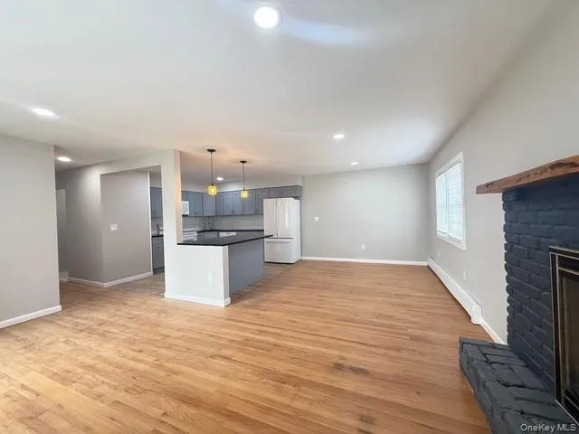 Kitchen with open floor plan, dark countertops, freestanding refrigerator, light wood-style flooring, and decorative light fixtures Kitchen with open floor plan, dark countertops, freestanding refrigerator, light wood-style flooring, and decorative light fixtures