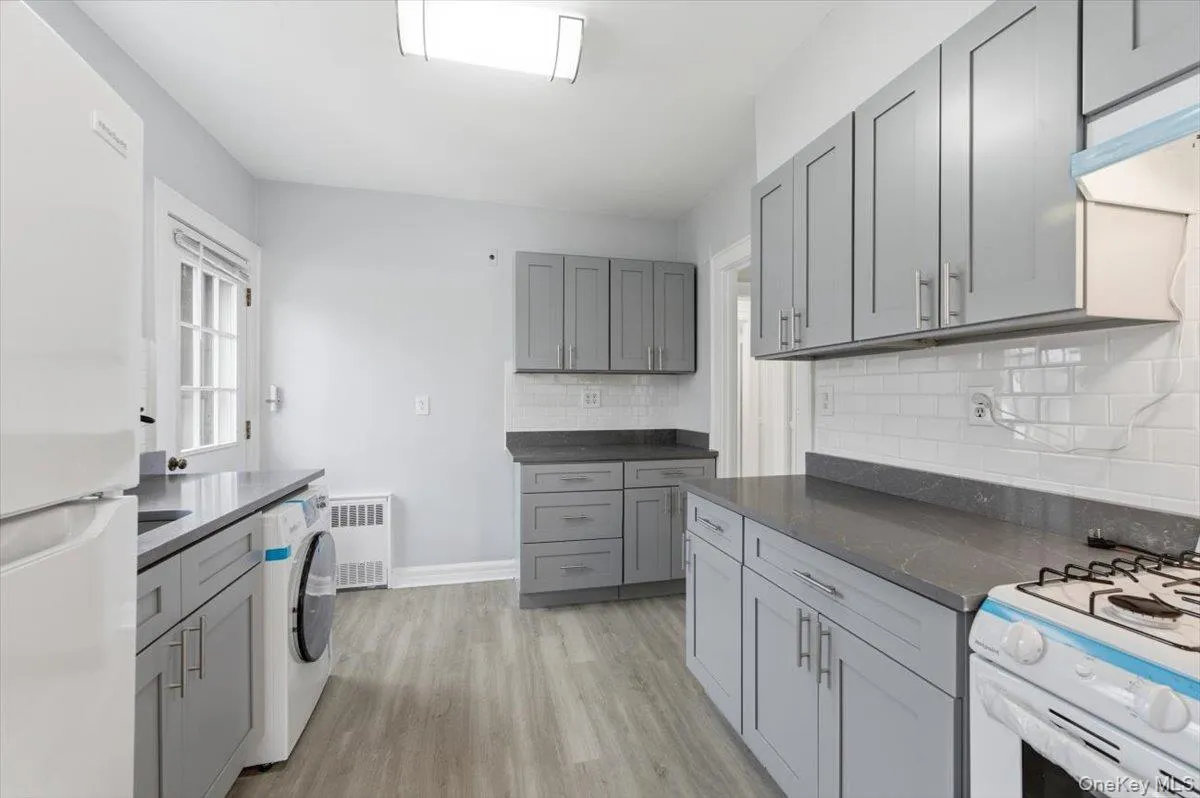 Kitchen featuring gray cabinetry, white appliances, light wood-type flooring, decorative backsplash, and washer / clothes dryer Kitchen featuring gray cabinetry, white appliances, light wood-type flooring, decorative backsplash, and washer / clothes dryer