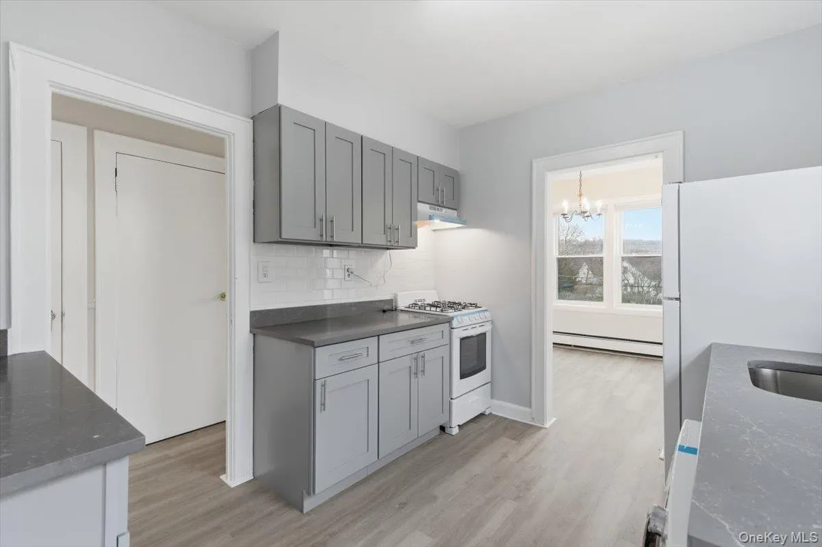 Kitchen with gray cabinets, white appliances, light wood-style flooring, baseboard heating, and decorative backsplash Kitchen with gray cabinets, white appliances, light wood-style flooring, baseboard heating, and decorative backsplash