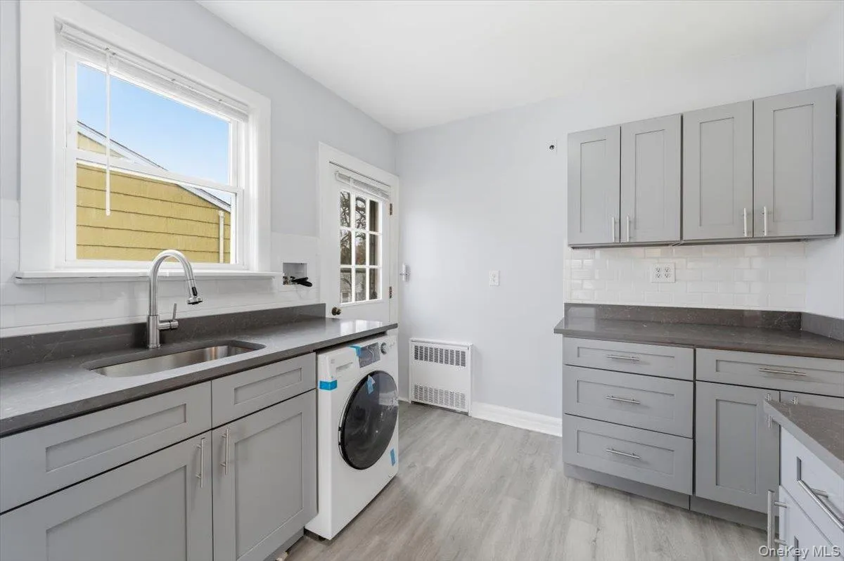Laundry area featuring washer / dryer, radiator heating unit, and light wood-style flooring Laundry area featuring washer / dryer, radiator heating unit, and light wood-style flooring