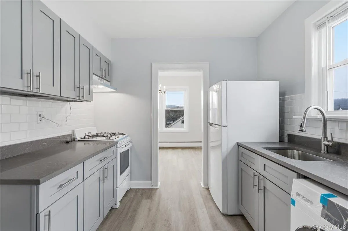 Kitchen with gray cabinetry, backsplash, white appliances, dark stone counters, and light wood-type flooring Kitchen with gray cabinetry, backsplash, white appliances, dark stone counters, and light wood-type flooring